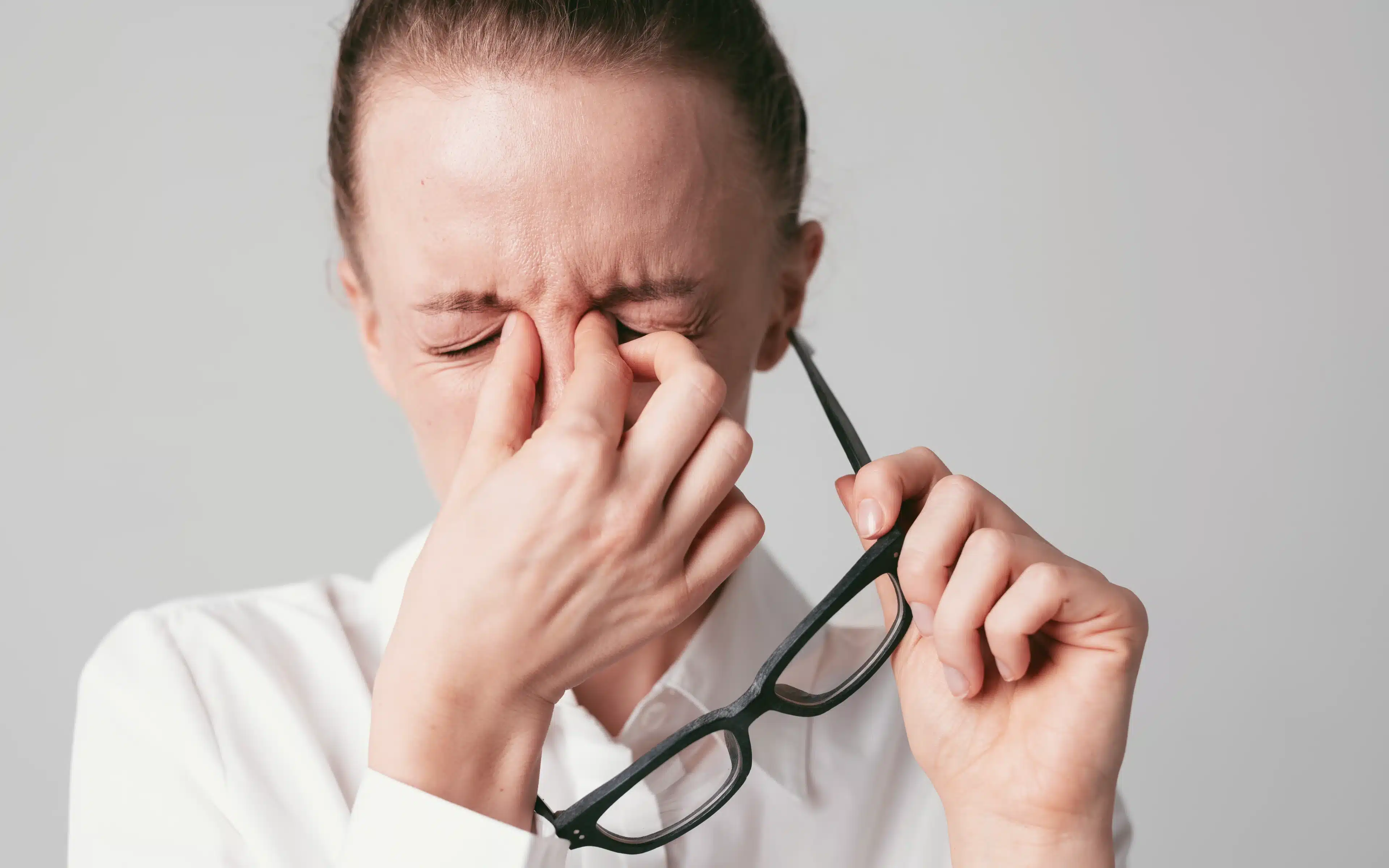 A female holding spectacles and rubbing her eyes.