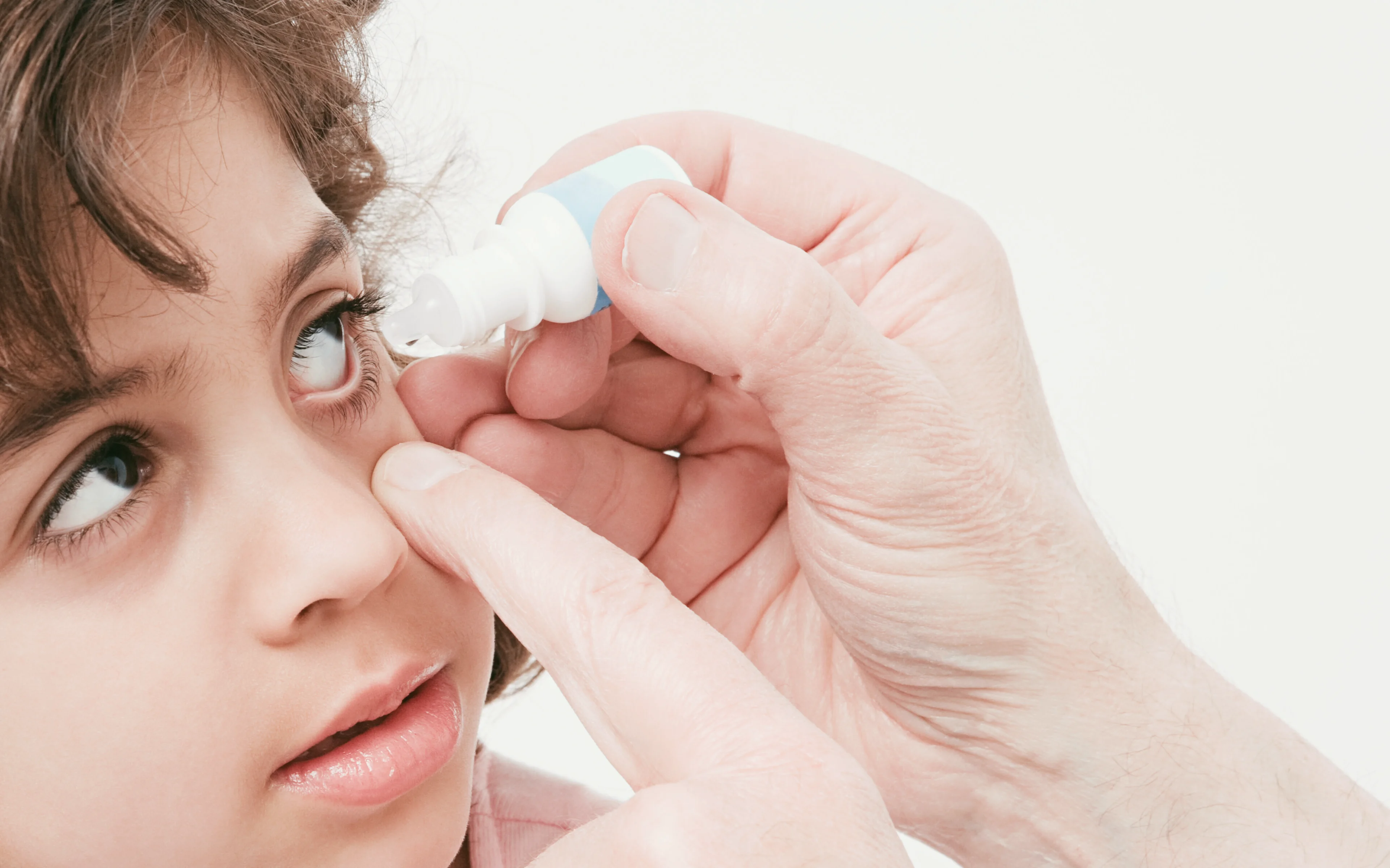 A female child has eye drops administered.