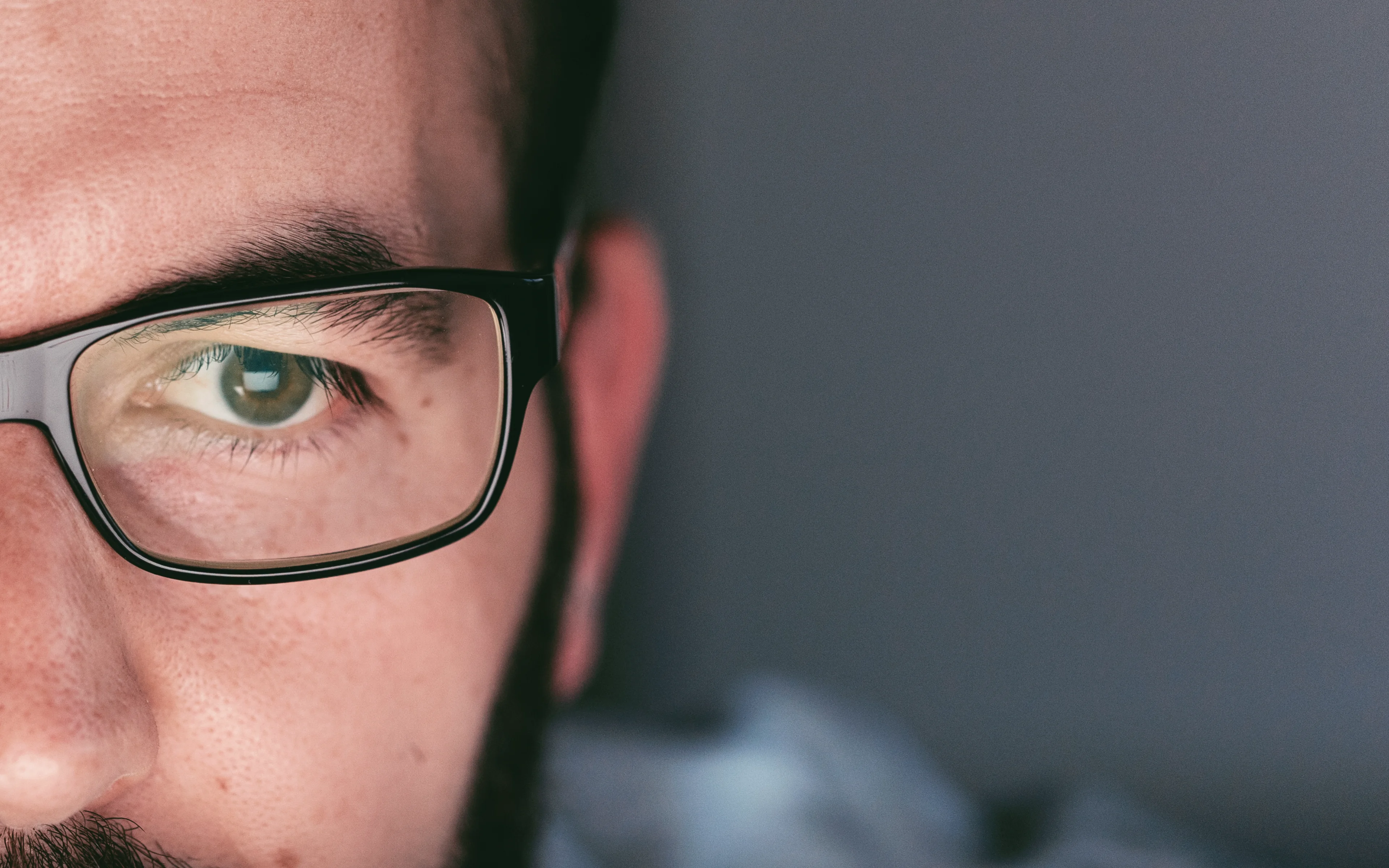 A male wearing glasses looking at a computer screen.