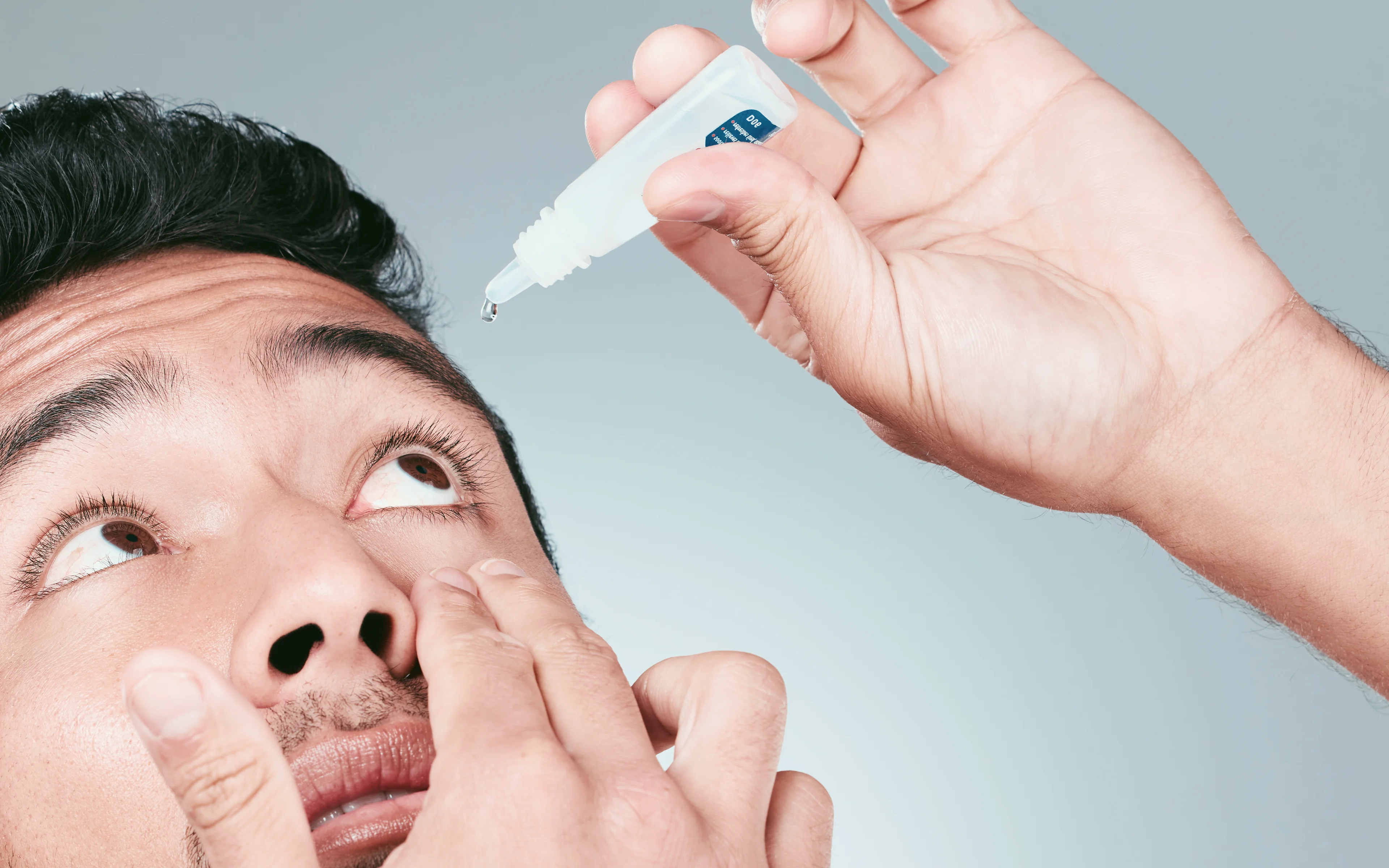 An Asian male using eye drops.