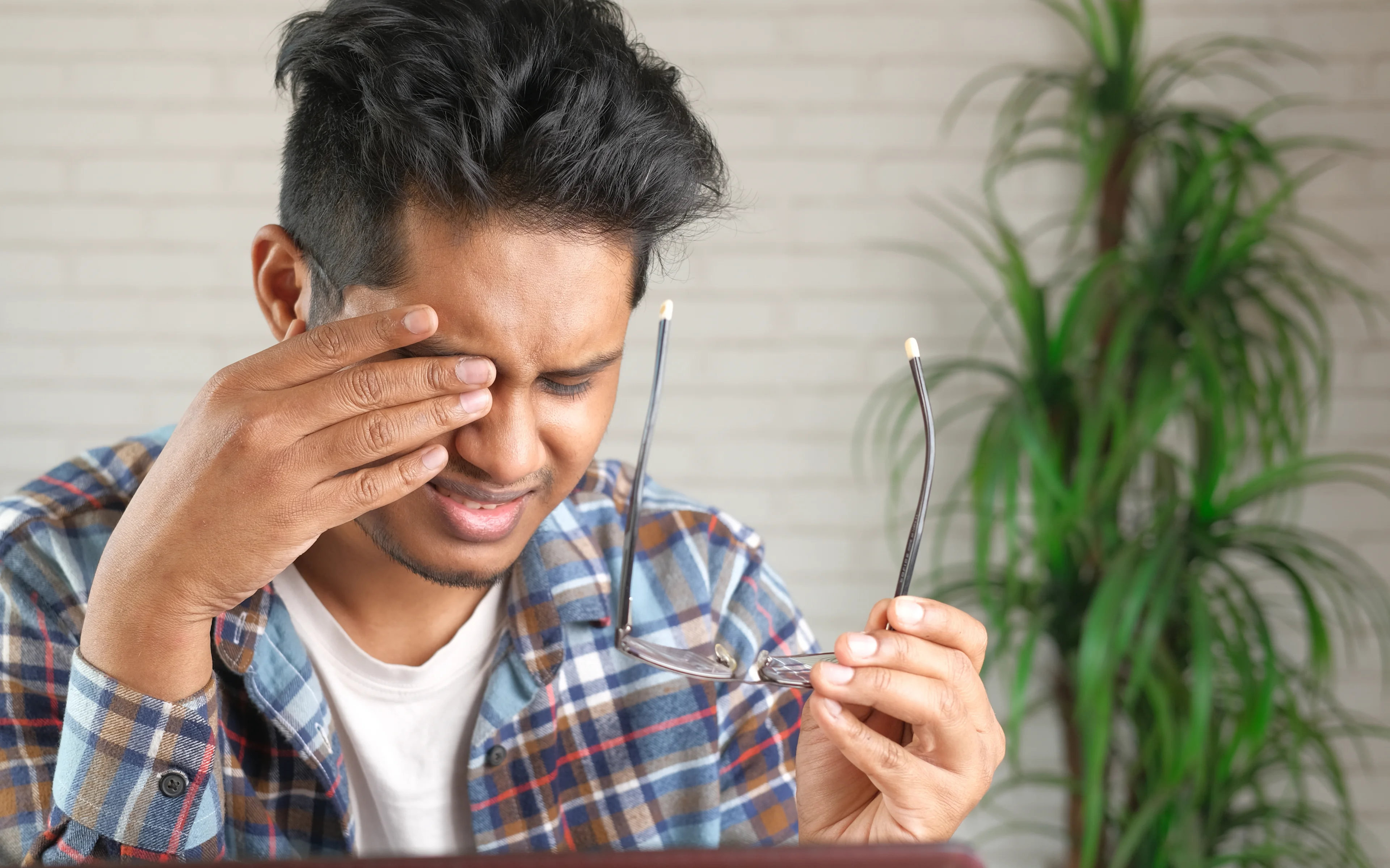 A young male rubs his eyes while holding glasses.