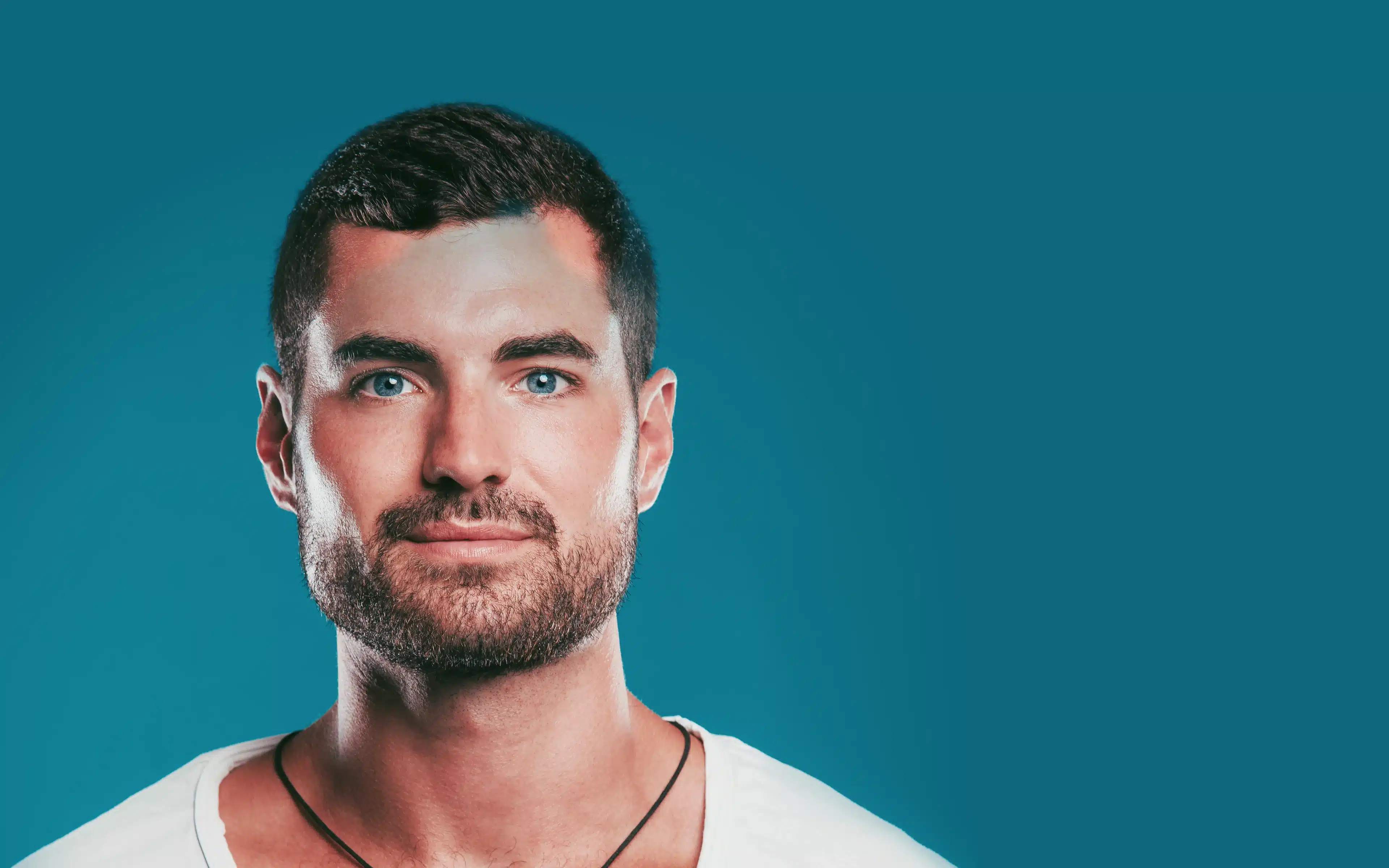 A stylish young man with blue eyes and beard, wearing contact lenses.