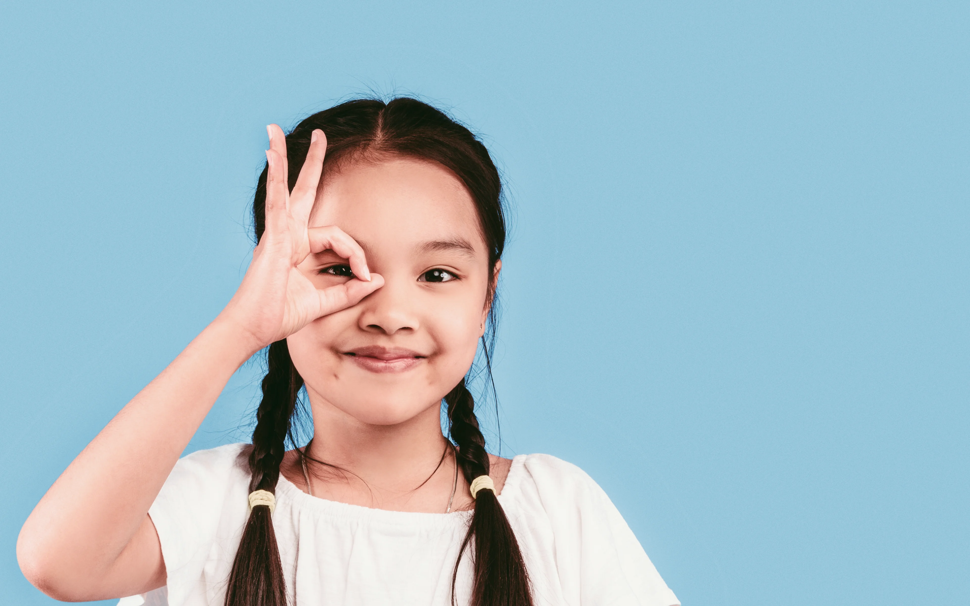Little girl looking through okay sign made with her hand.