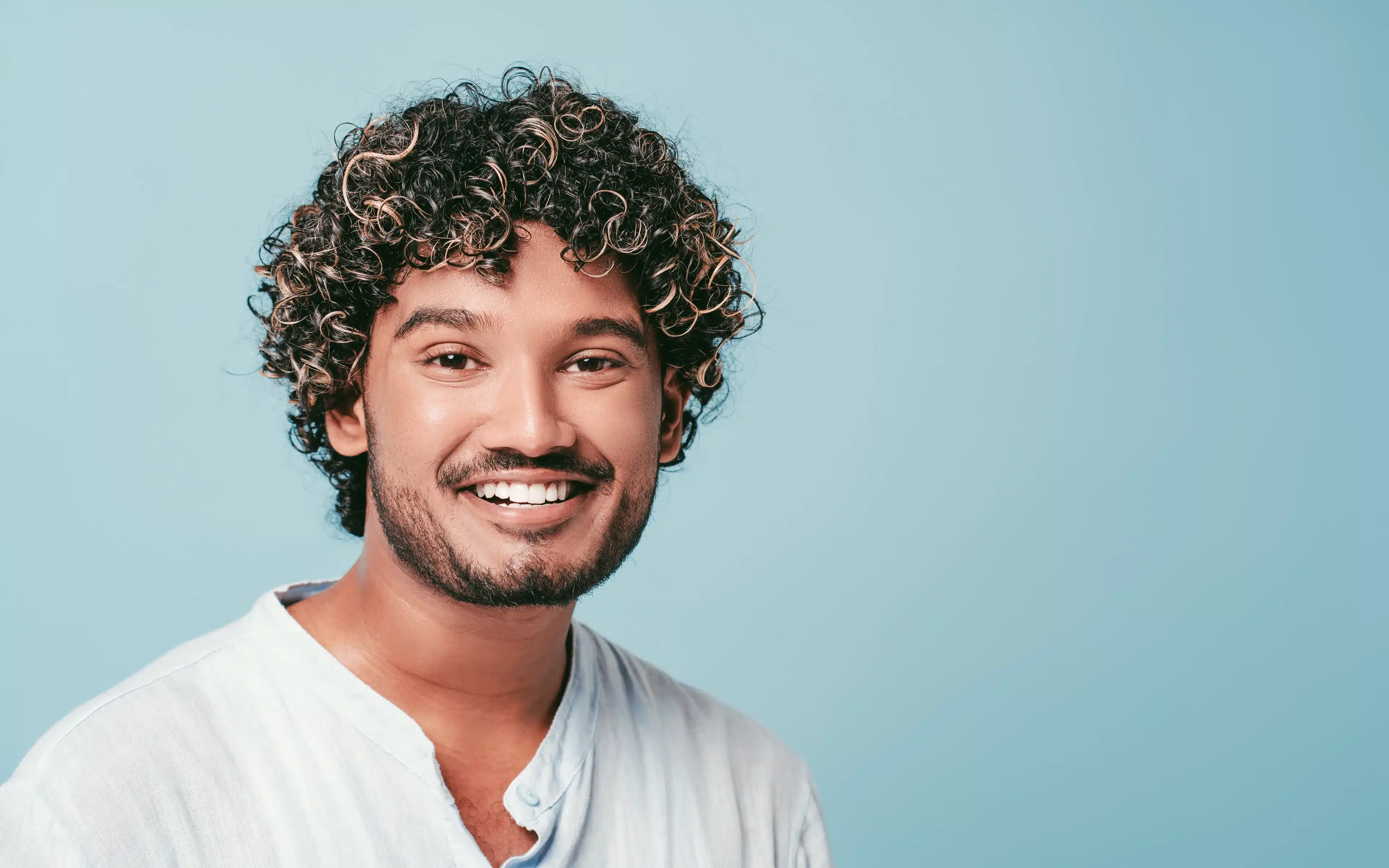 Young man with curly hair smiles happily, wearing scleral contact lenses.