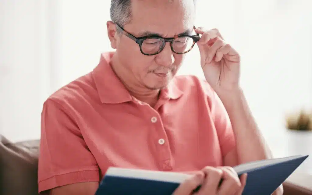 A male adjusts his glasses while reading a book.