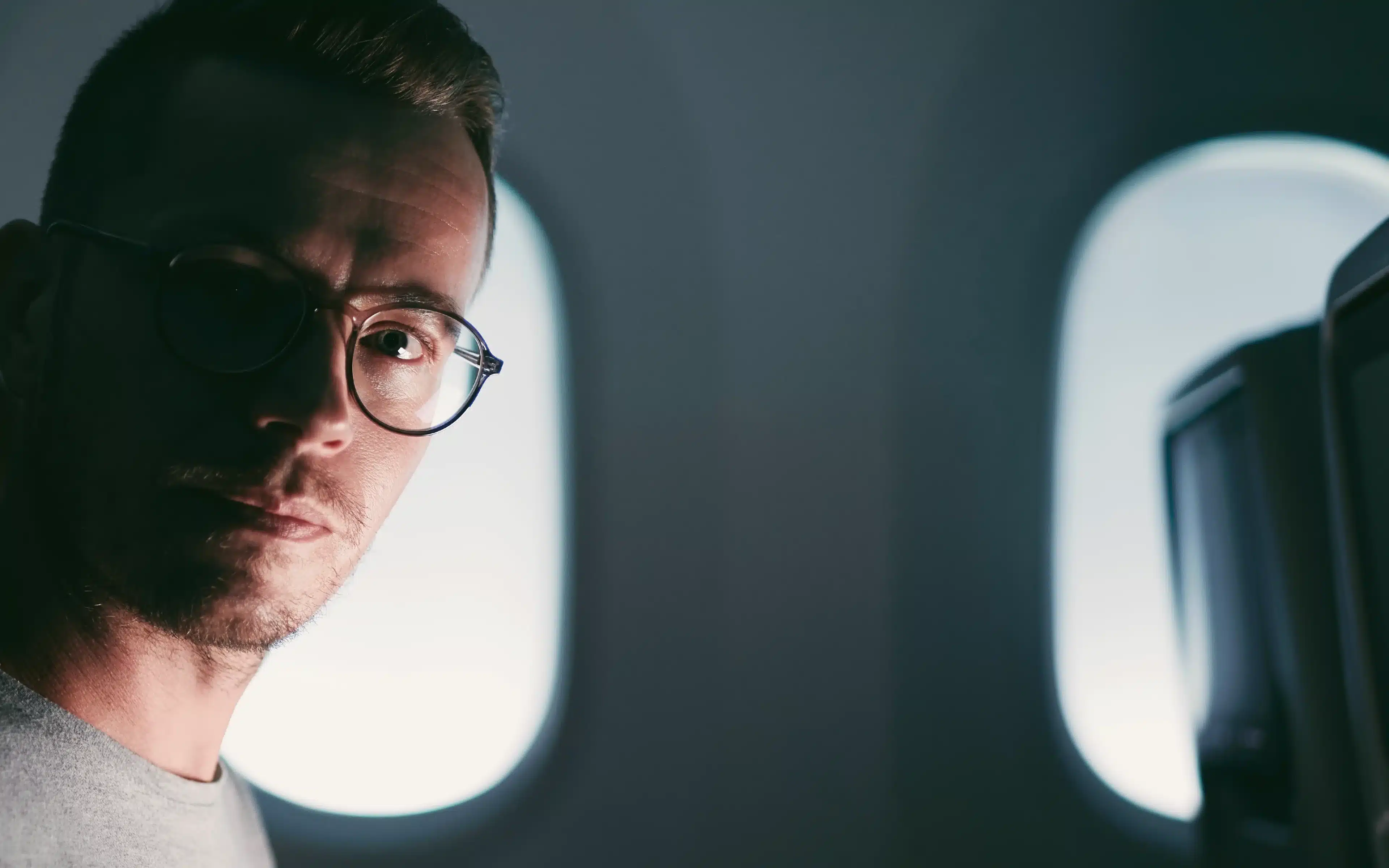 A male passenger wearing glasses in an aeroplane.