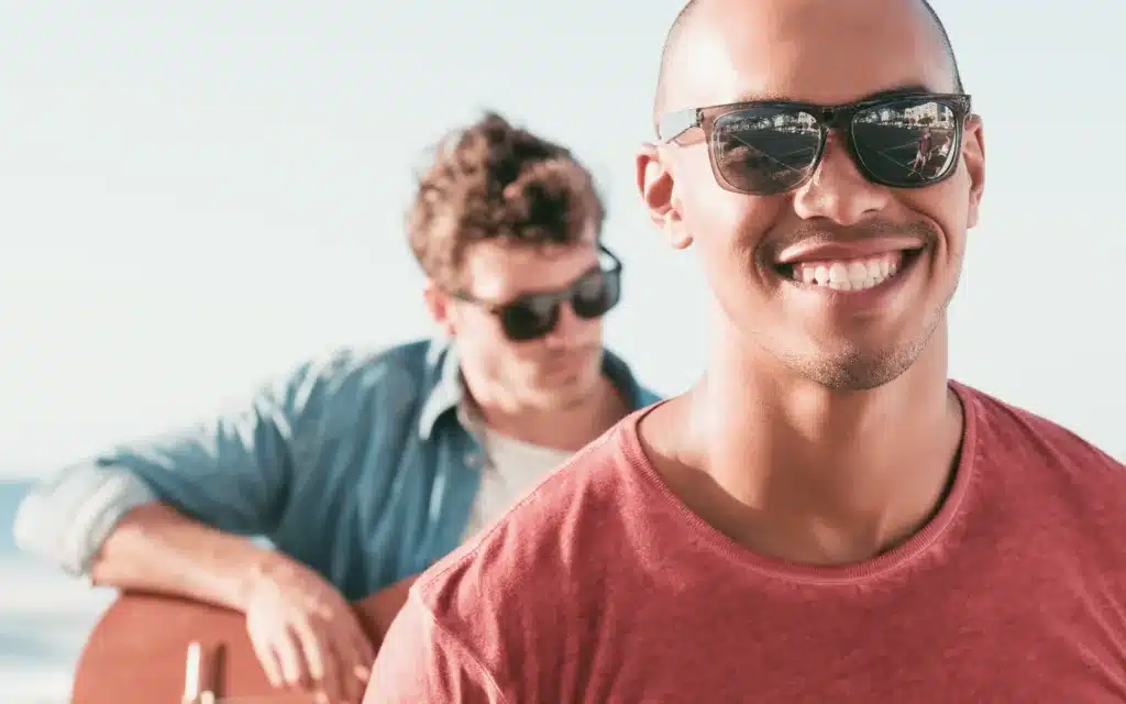 Portrait Of A Smiling Man Wearing Sunglasses In Front Of Man Playing Guitar.