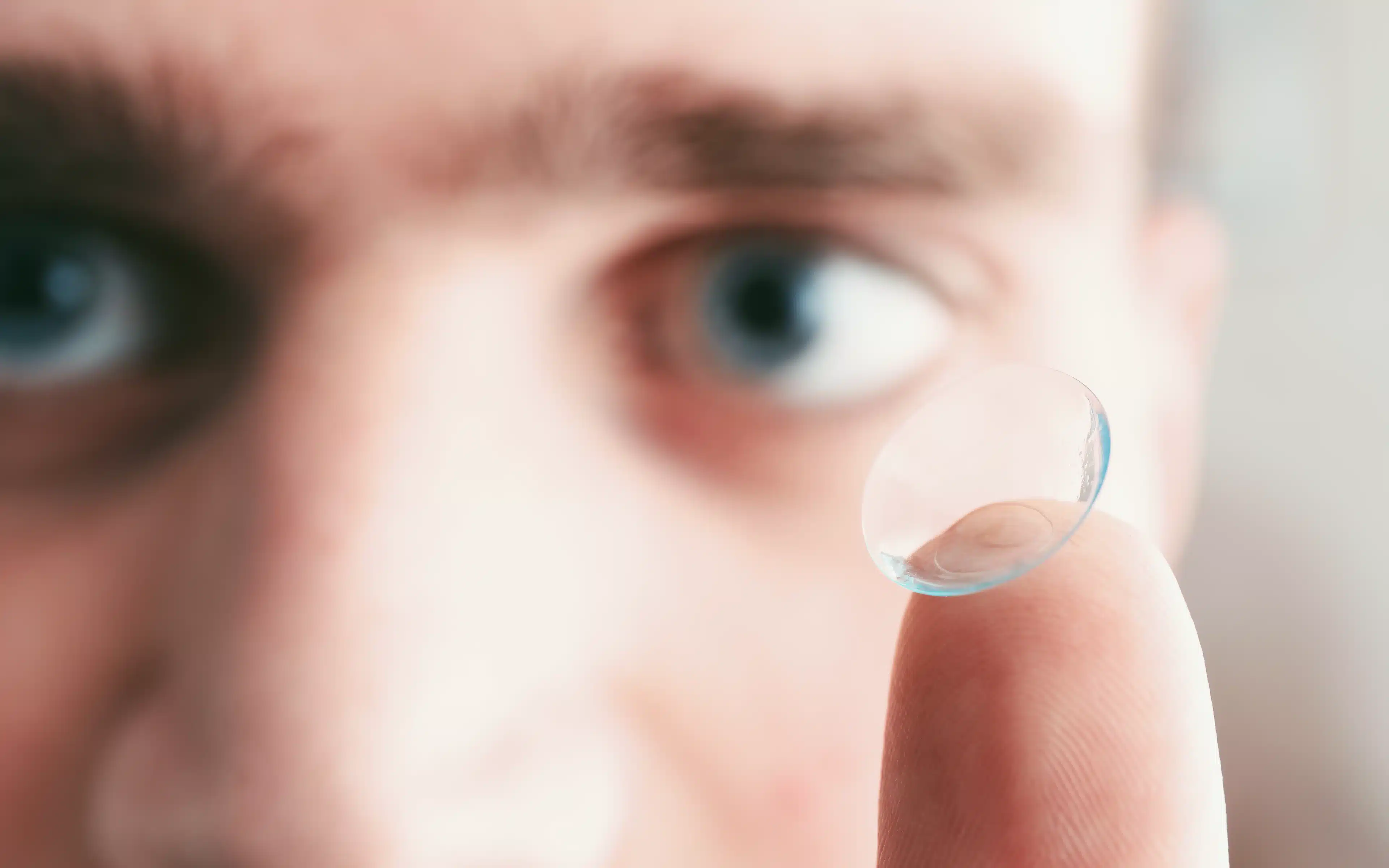 Man with blue eyes and contact lens on finger, close up