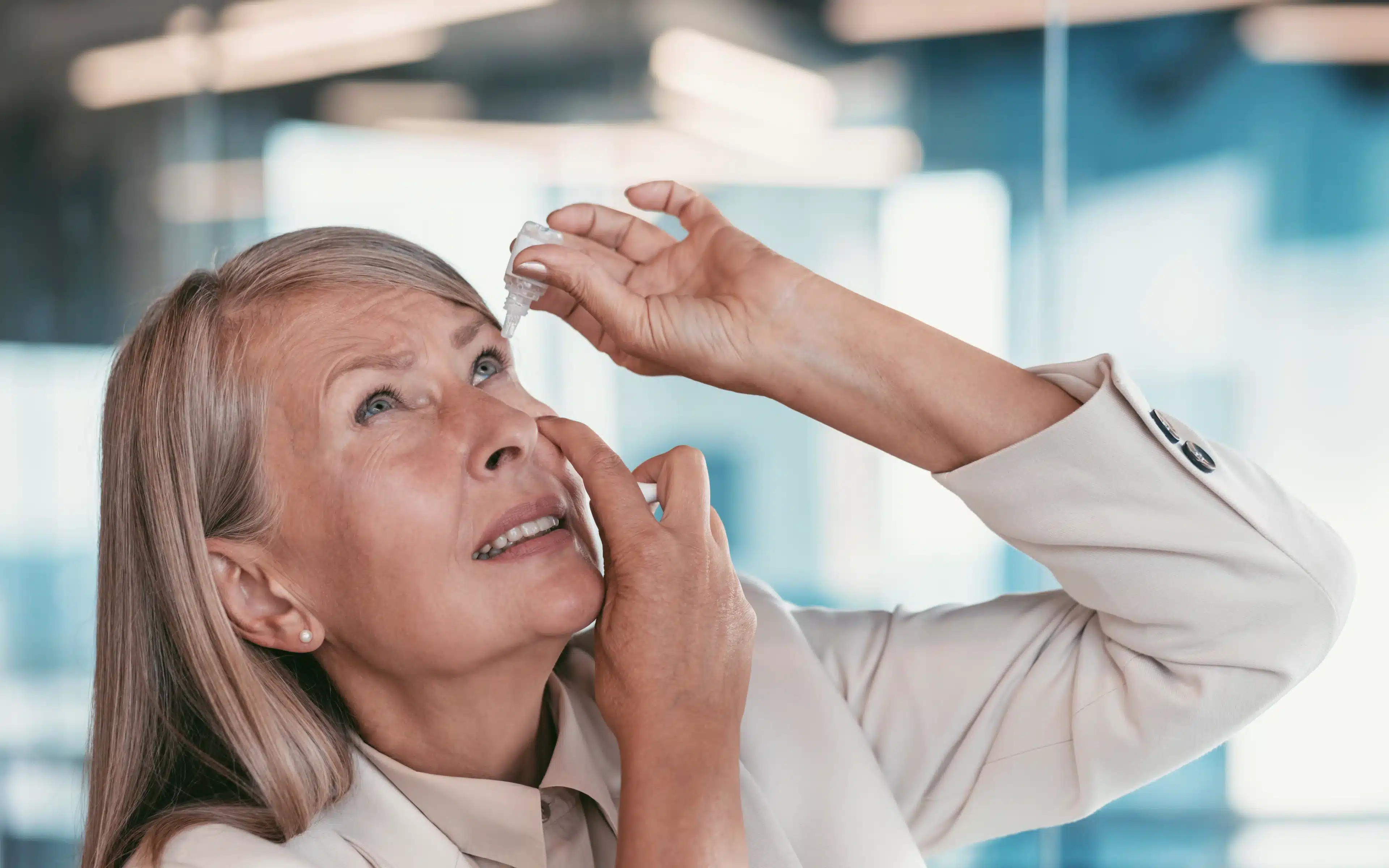 Mature woman applying lubricating eye drops to treat dry eyes from rosacea