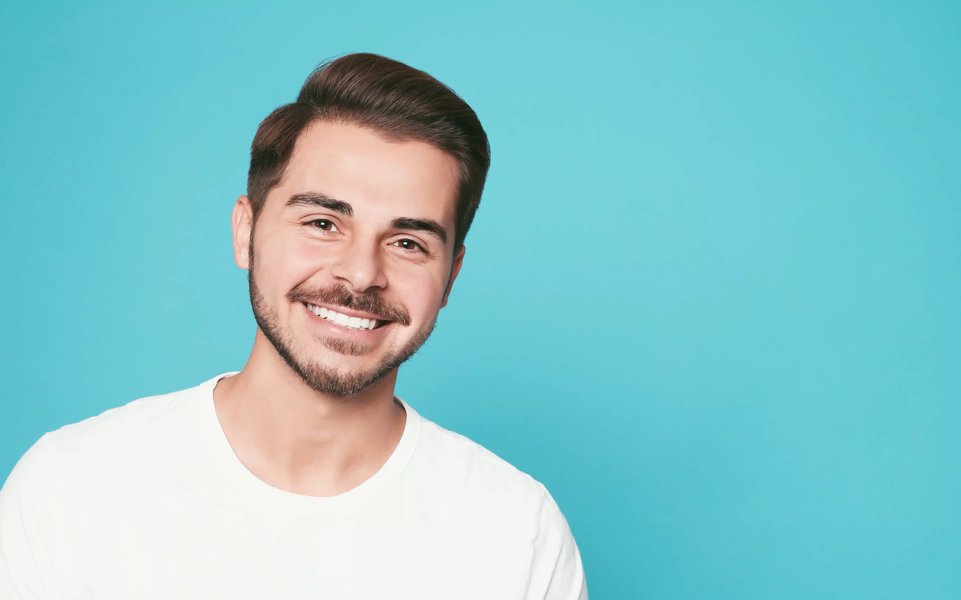 A smiling young man against a teal background, representing good health and wellbeing