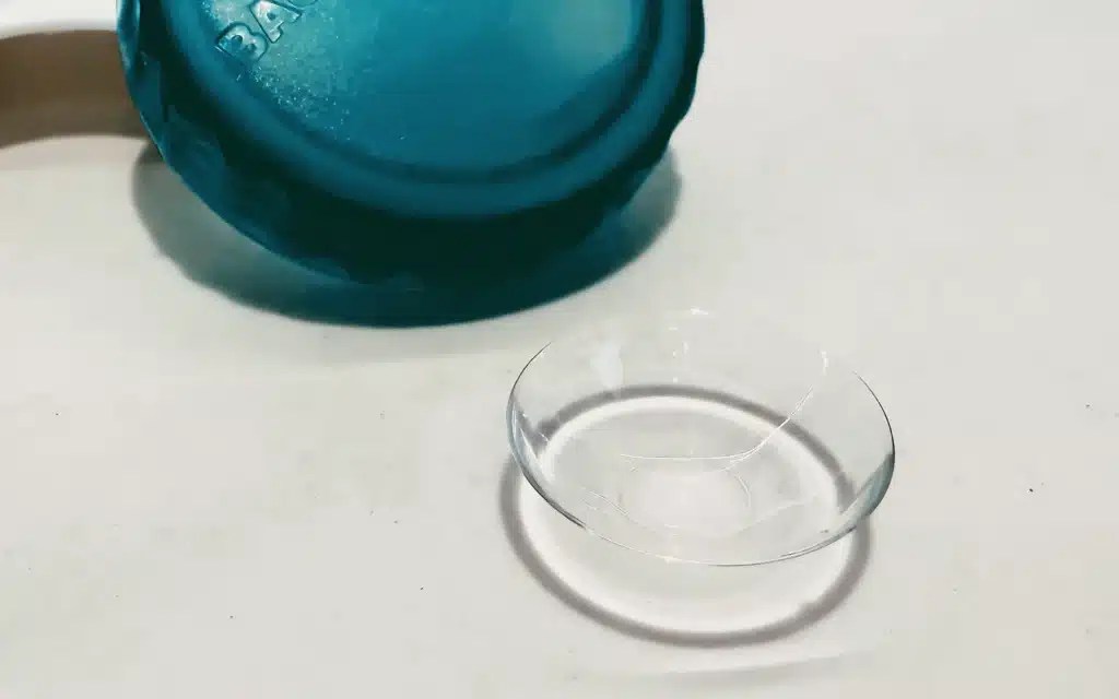 Clear scleral contact lens beside open teal storage case on white surface